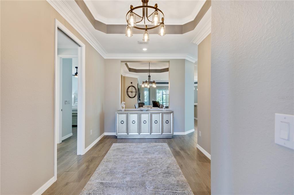 A hallway with a tray ceiling, chandelier, mirrored console table, and a patterned area rug — 12584 WELLEN GOLF STREET, VENICE, FL