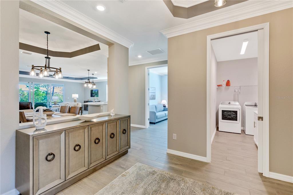 A hallway with a wooden console table leads to a laundry room and living area — 12584 WELLEN GOLF STREET, VENICE, FL