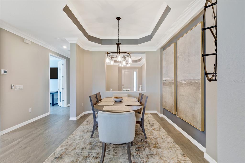 A dining room features a tray ceiling, a chandelier, a wooden table, and wall art — 12584 WELLEN GOLF STREET, VENICE, FL