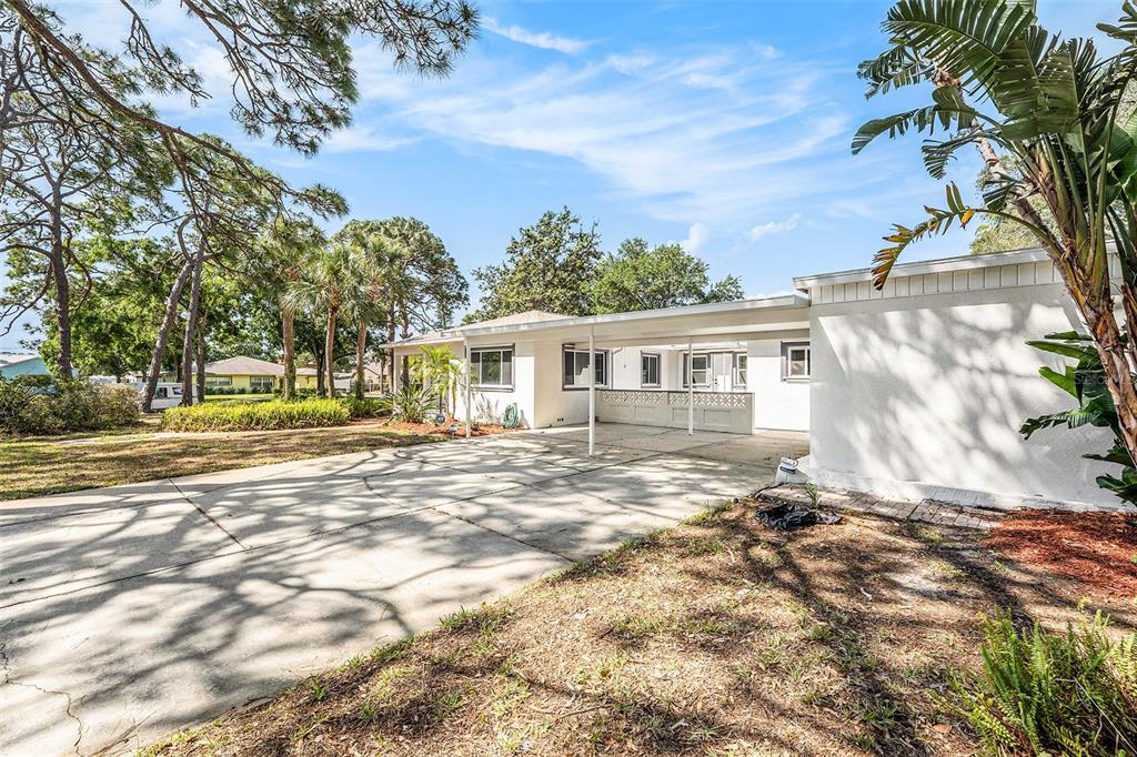 A white single-story house features a large concrete driveway and an attached covered carport — 4925 ALCAZAR WAY S, ST PETERSBURG, FL