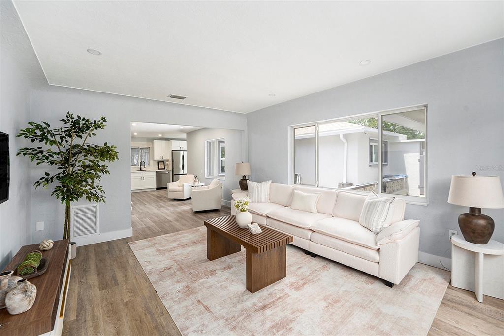 A living room with light wood flooring, a white sofa, and an adjacent kitchen — 4925 ALCAZAR WAY S, ST PETERSBURG, FL
