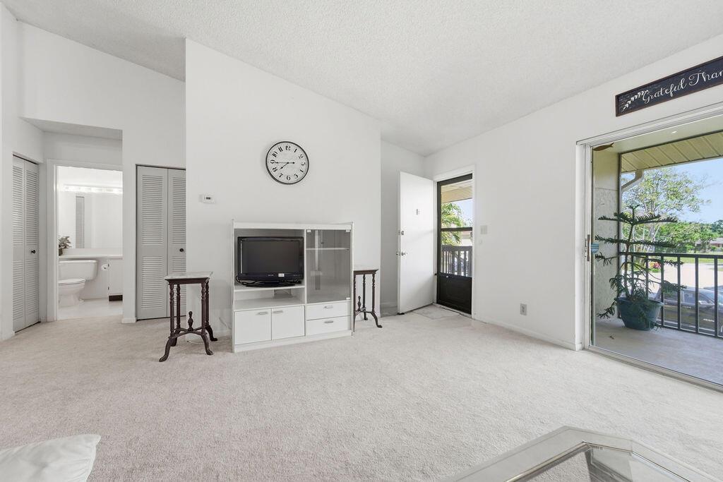 A living room with white walls, beige carpeting, a television stand, and a sliding glass door — 6519 Chasewood Drive, Jupiter FL 33458, JUPITER, FL