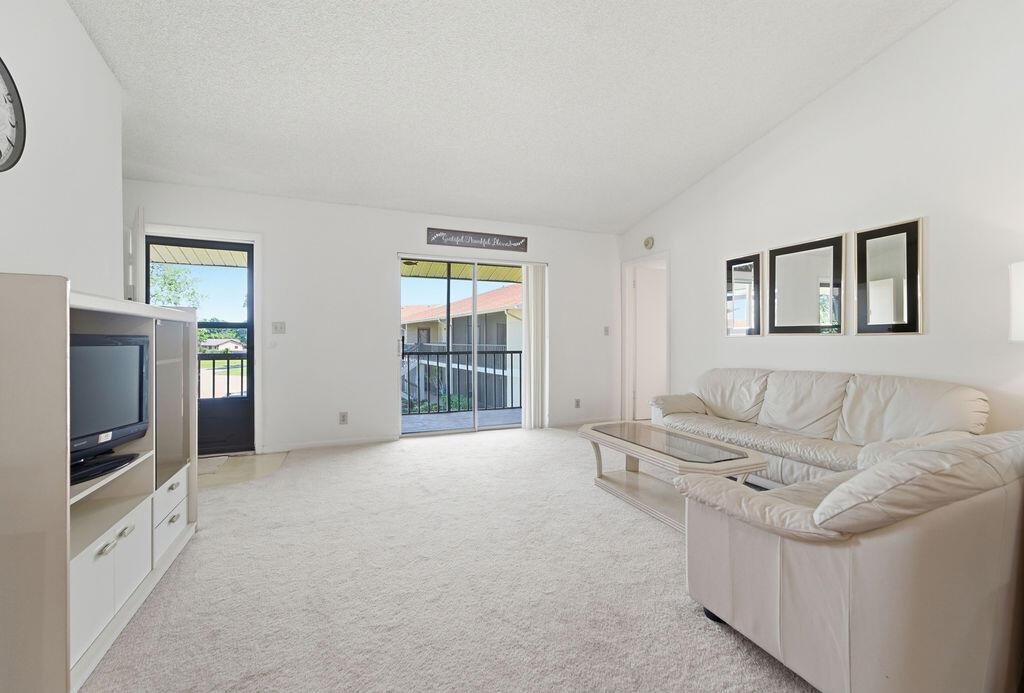 A living room features white walls, beige carpeting, a white sofa, and a sliding glass door — 6519 Chasewood Drive, Jupiter FL 33458, JUPITER, FL