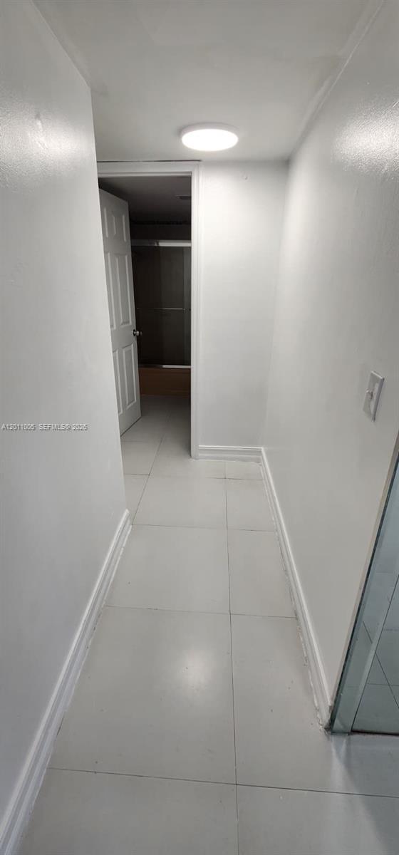 A narrow hallway with white walls and light-colored tile flooring leads to a bathroom doorway — 1020 NW 80th Ave # 203, Margate FL 33063, MARGATE, FL