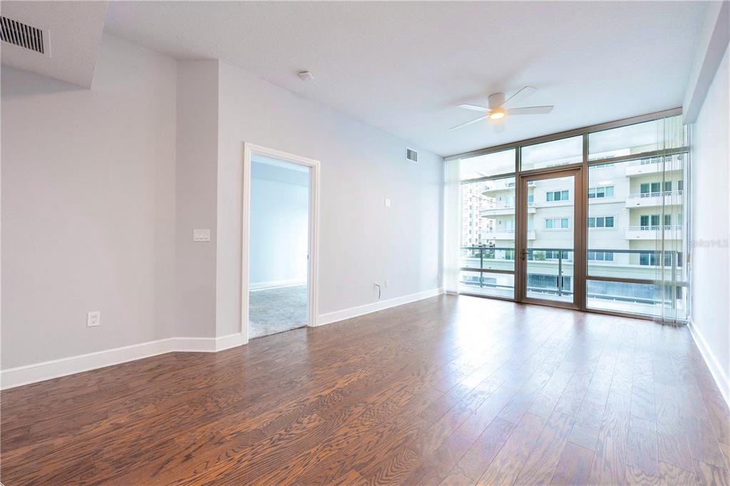 An empty living room features hardwood floors, a ceiling fan, and floor-to-ceiling windows with balcony access — 101 S EOLA DRIVE UNIT 614, ORLANDO, FL