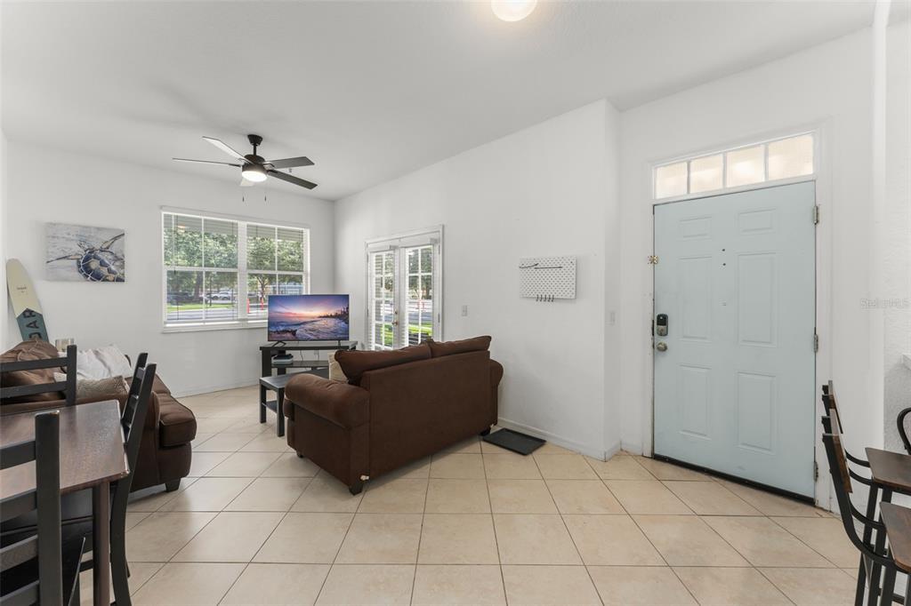 A living room with tile flooring, a brown sofa, a television, and a light blue door — 4000 VENETIAN BAY DRIVE UNIT 107, KISSIMMEE, FL