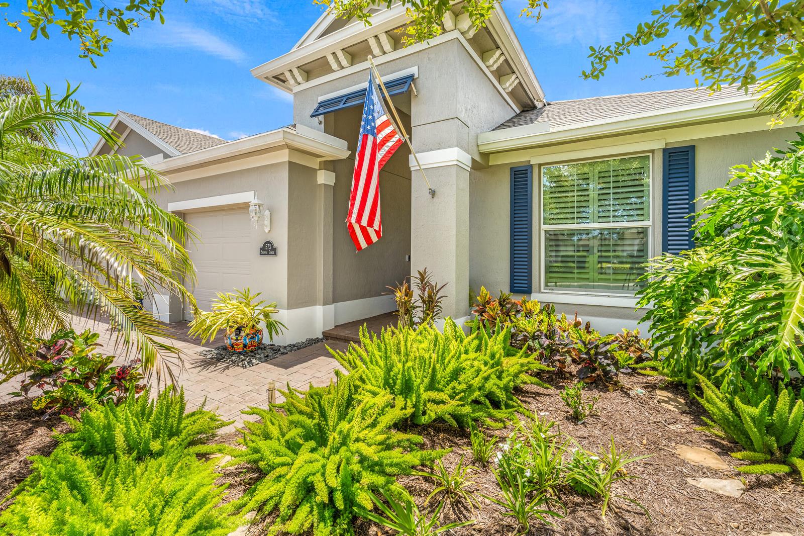 A single-story house with a gray exterior, blue shutters, a front flag, and landscaped yard — 1573 Segovia Circle, Vero Beach FL 32966, VERO BEACH, FL