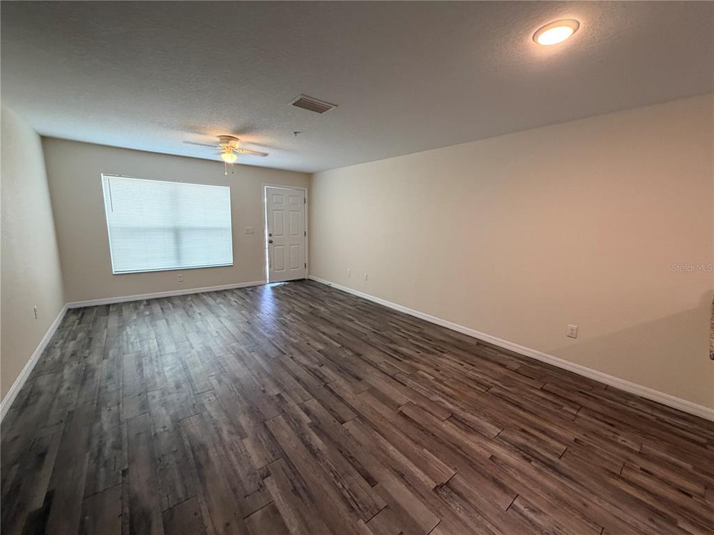 An empty living room features wood-look flooring, beige walls, a ceiling fan, and an entry door — 8532 JUNIPER ROAD UNIT 2, OCALA, FL