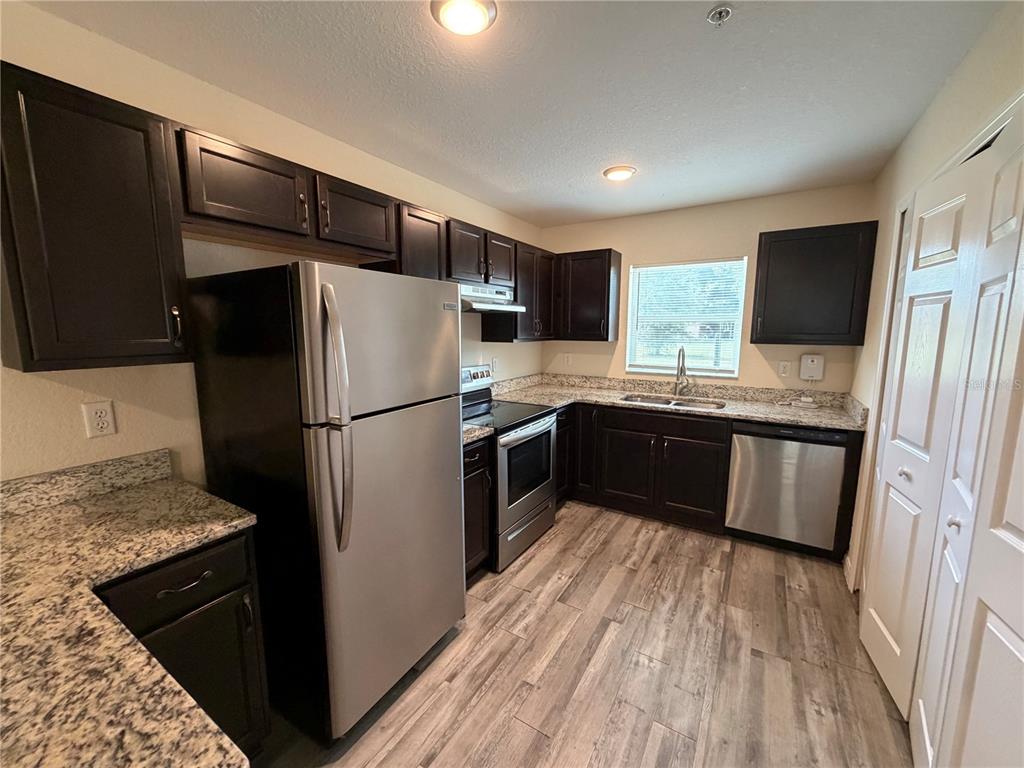 A kitchen features dark wood cabinets, granite countertops, stainless steel appliances, and wood-look flooring — 8532 JUNIPER ROAD UNIT 2, OCALA, FL
