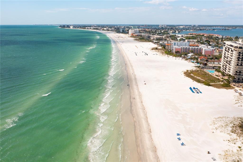 An aerial view shows a wide white sand beach bordering turquoise ocean waters and buildings — 3805 GULF BOULEVARD UNIT 203, ST PETE BEACH, FL
