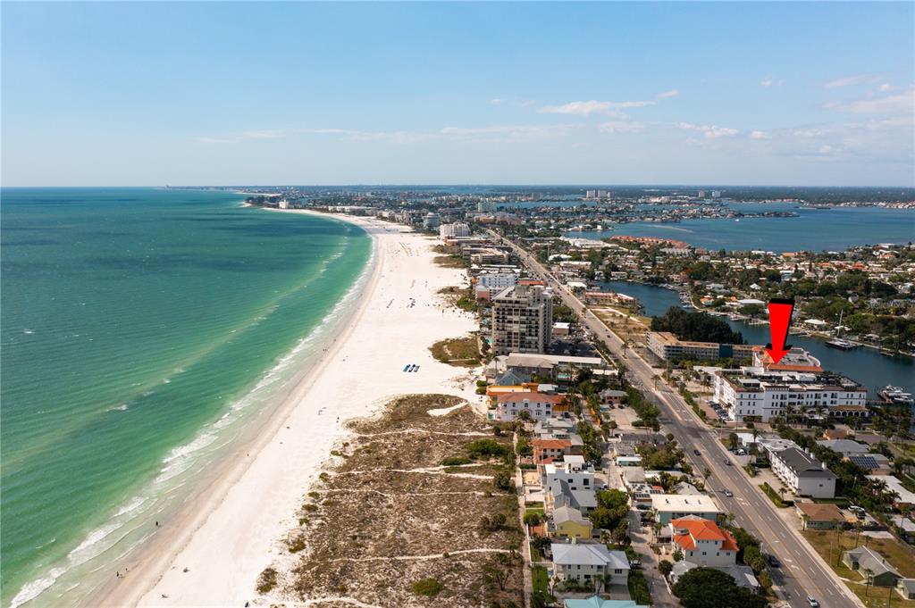 An aerial view shows a coastal beach town with a red arrow pointing to a building — 3805 GULF BOULEVARD UNIT 203, ST PETE BEACH, FL