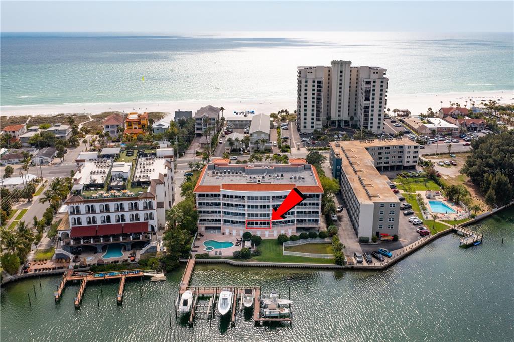 An aerial view shows a multi-story waterfront condominium building with a red arrow pointing to a balcony — 3805 GULF BOULEVARD UNIT 203, ST PETE BEACH, FL