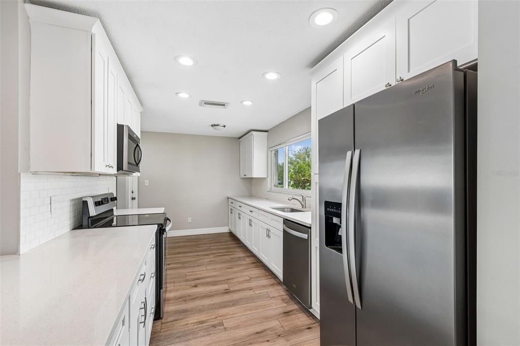 A kitchen features white cabinets, stainless steel appliances, quartz countertops, and wood-look flooring — 1943 BARBARA AVENUE, CLEARWATER, FL