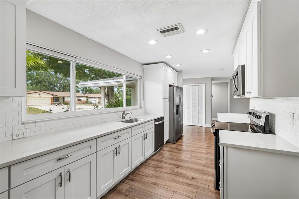 A modern kitchen features white cabinets, stainless steel appliances, a breakfast bar, and wood flooring — 1943 BARBARA AVENUE, CLEARWATER, FL