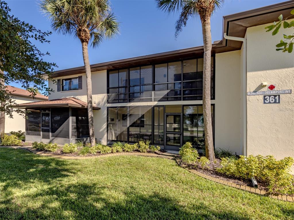 A two-story building features a screened-in patio and balcony surrounded by palm trees and landscaping — 361 AIRPORT AVENUE E UNIT 508, VENICE, FL