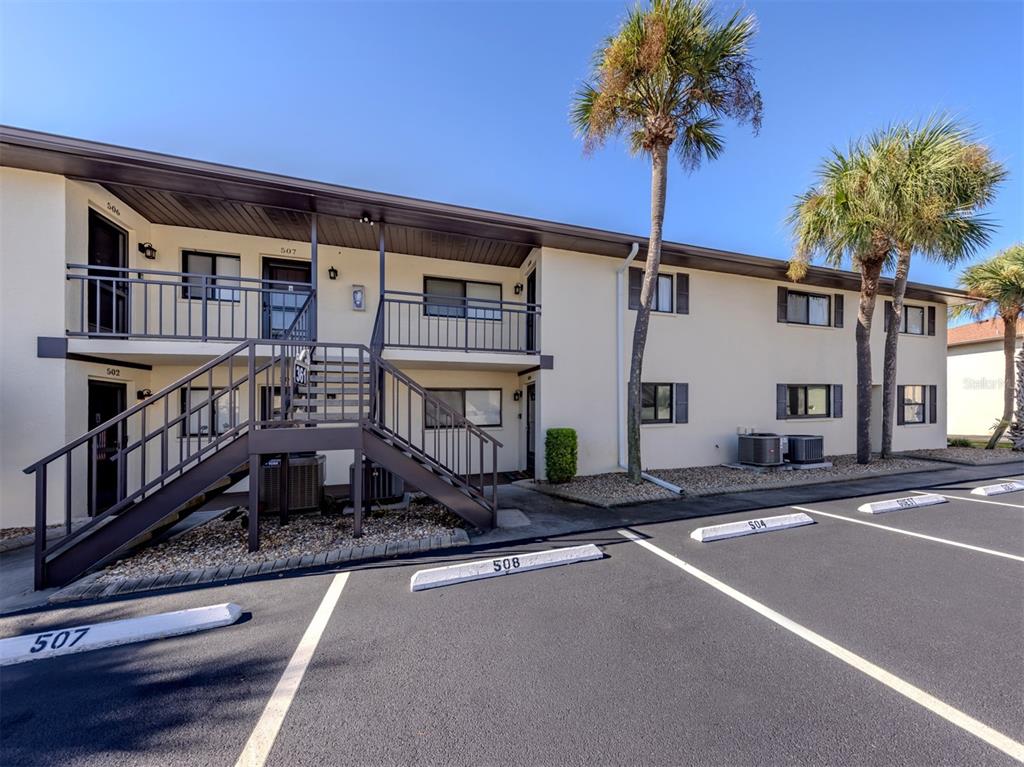 A two-story apartment building exterior features a metal staircase, parking spaces, and palm trees — 361 AIRPORT AVENUE E UNIT 508, VENICE, FL