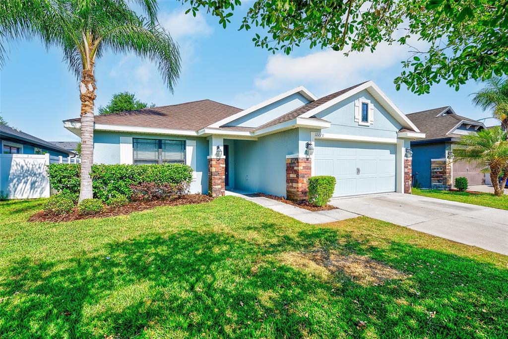 A light blue single-story house features a two-car garage, stone accents, and a palm tree — 12220 LEGACY BRIGHT STREET, RIVERVIEW, FL