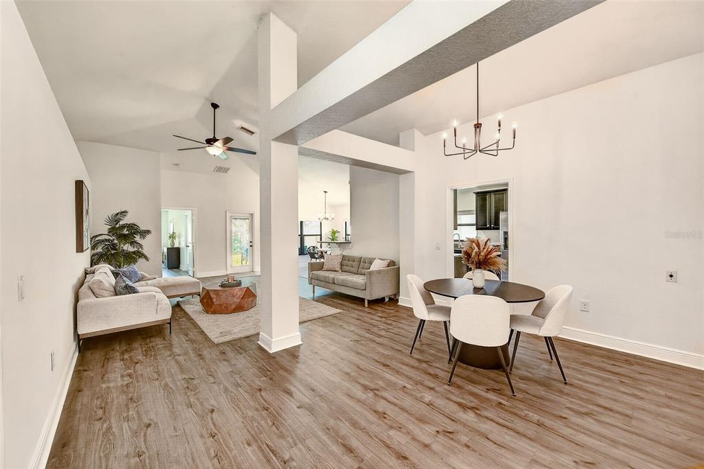 An open-concept living and dining area features wood-look flooring, white walls, and vaulted ceilings — 12220 LEGACY BRIGHT STREET, RIVERVIEW, FL