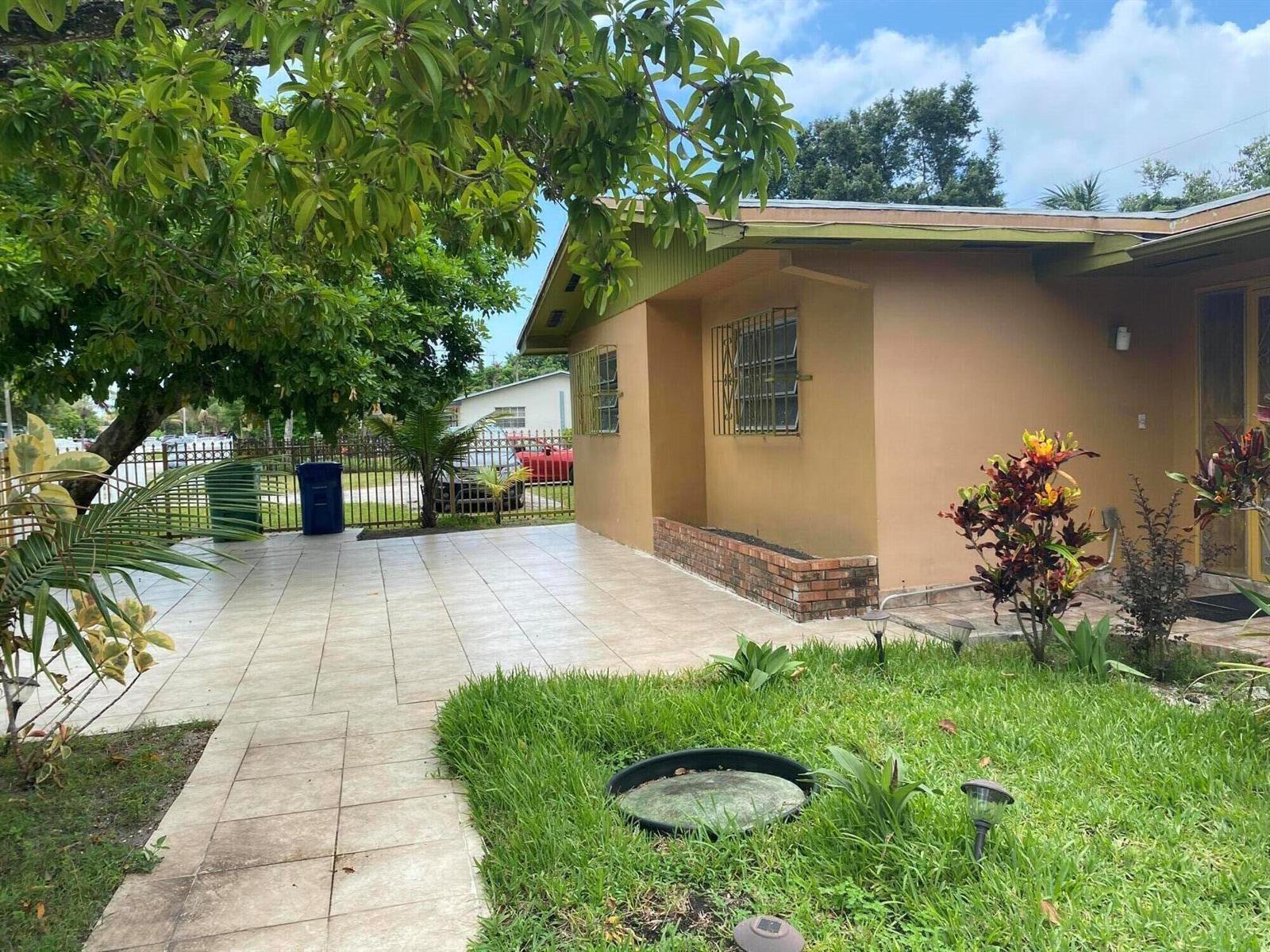 A tan house exterior features a tiled patio, a brick planter, and a grassy yard — 1050 NW 100th Street, Miami FL 33150, MIAMI, FL