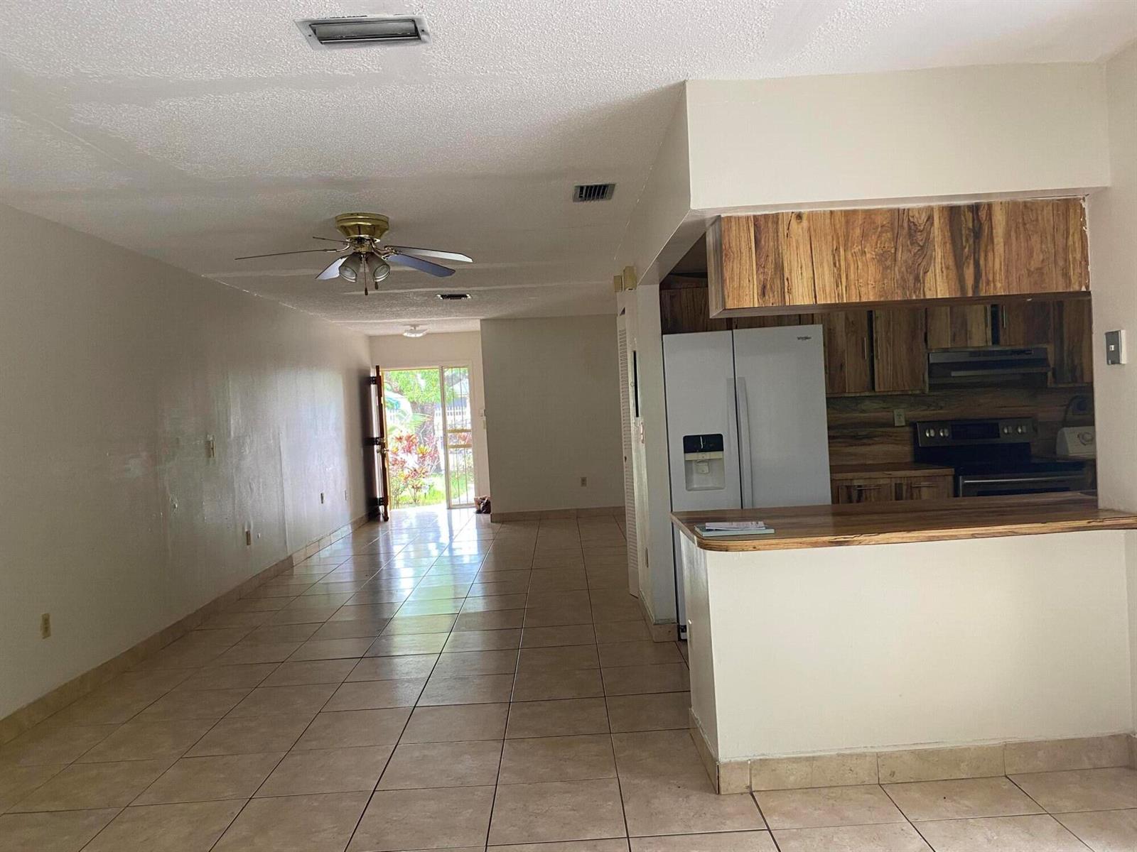 An open-concept living area with tile floors leads to a kitchen with wood-toned cabinets — 1050 NW 100th Street, Miami FL 33150, MIAMI, FL