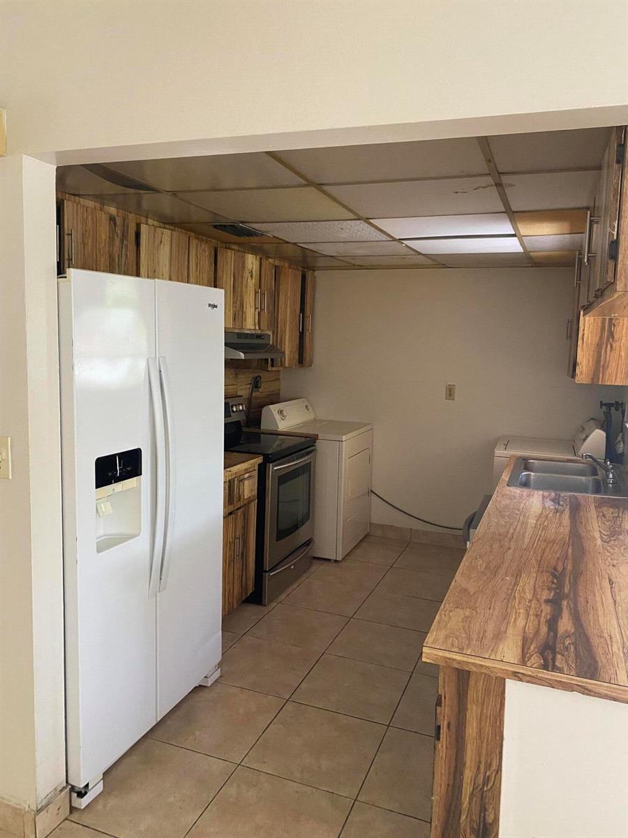 A kitchen with wood-grain cabinets, a white refrigerator, stainless steel stove, and tiled flooring — 1050 NW 100th Street, Miami FL 33150, MIAMI, FL