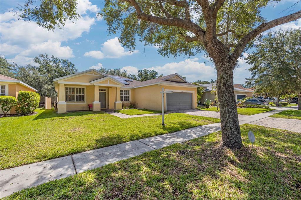 A single-story yellow house with a two-car garage and a large tree in the yard — 11328 BRIDGE PINE DRIVE, RIVERVIEW, FL