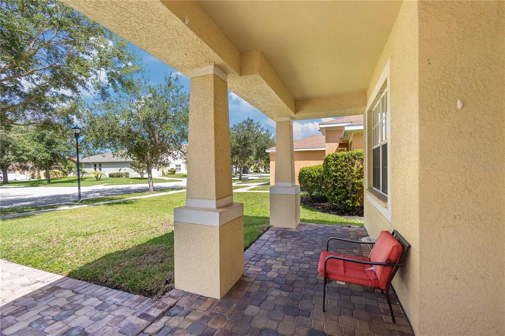 A covered front porch with paver flooring, two stucco columns, and a red patio chair — 11328 BRIDGE PINE DRIVE, RIVERVIEW, FL
