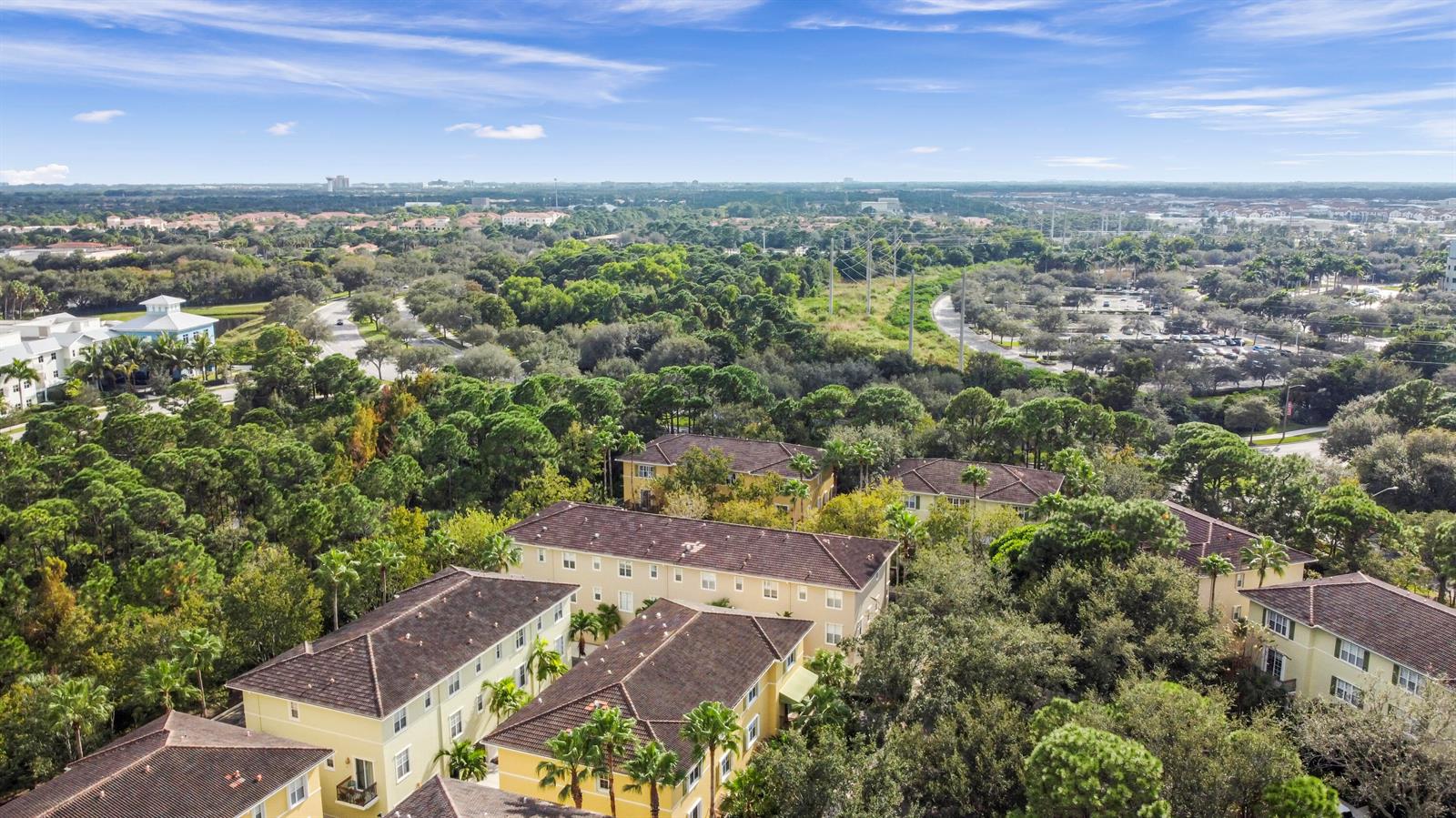 An aerial view shows several multi-story yellow apartment buildings surrounded by dense green trees — 148 E Morning Dew Circle, Jupiter FL 33458, JUPITER, FL