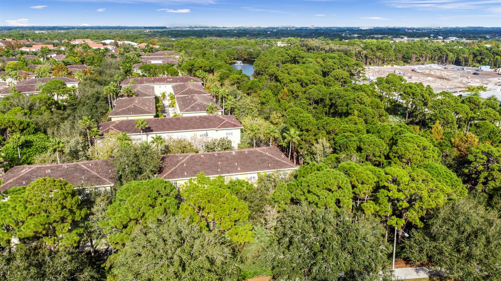 An aerial view shows multi-story apartment buildings nestled among dense trees near a small lake — 148 E Morning Dew Circle, Jupiter FL 33458, JUPITER, FL