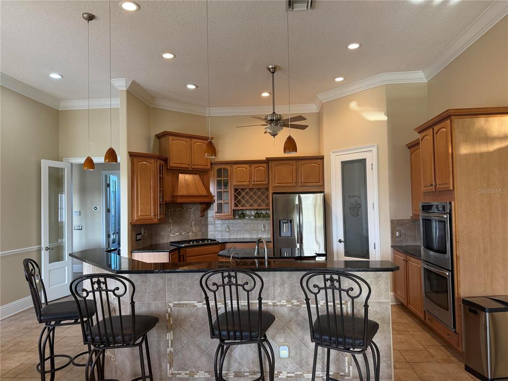 A kitchen features wood cabinets, granite countertops, a breakfast bar with stools, and stainless appliances — 2120 BUNKER VIEW COURT, KISSIMMEE, FL