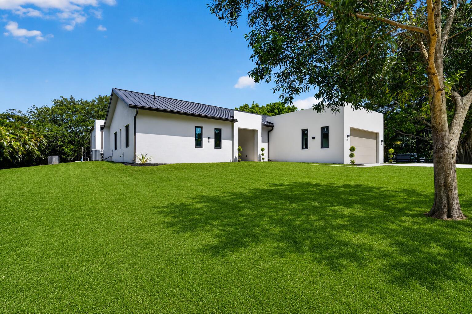 A modern white house with a dark metal roof sits on a large green lawn — 5356 Colbright Road, Lake Worth FL 33467, LAKE WORTH, FL