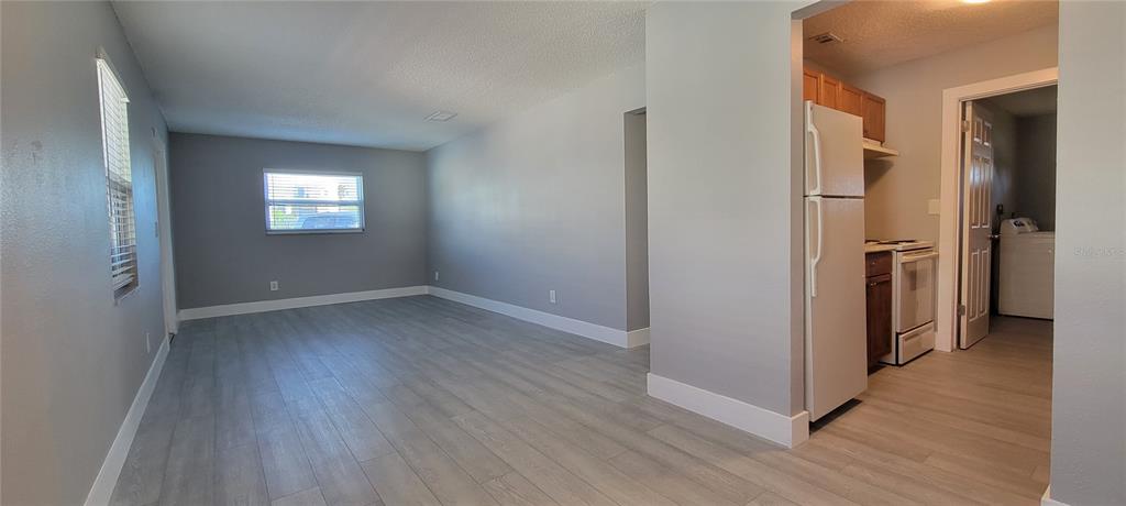 A living room with light gray walls and wood-look flooring opens into a small kitchen — 6627 S WEST SHORE BOULEVARD, TAMPA, FL