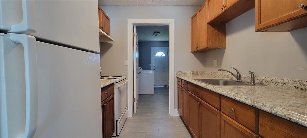 A kitchen with wood cabinets, granite countertops, and a white refrigerator leads to a laundry room — 6627 S WEST SHORE BOULEVARD, TAMPA, FL