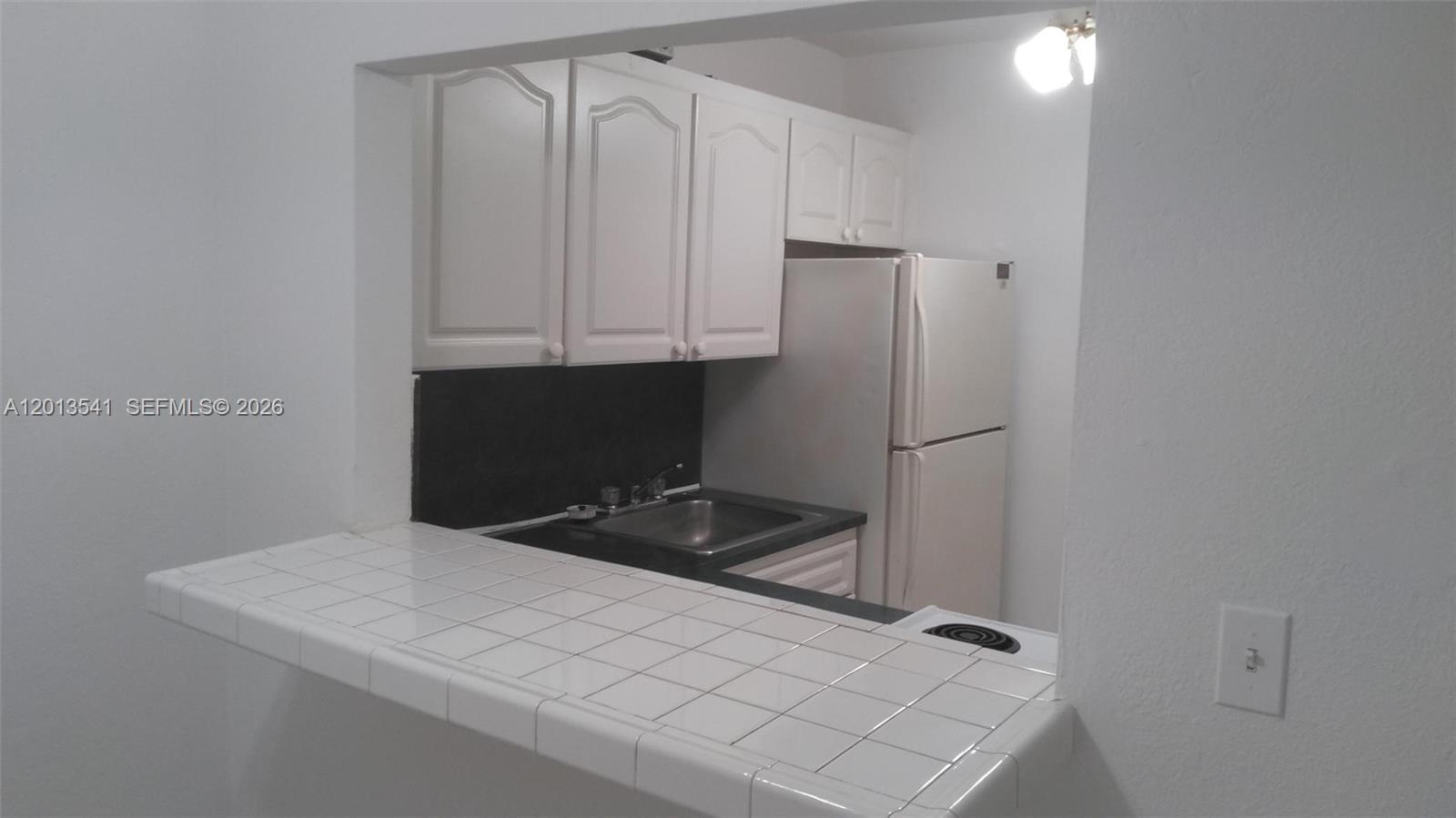 A small kitchen features white cabinets, a black countertop, and a tiled breakfast bar — 1441 Lincoln Rd # 414, Miami Beach FL 33139, MIAMI BEACH, FL