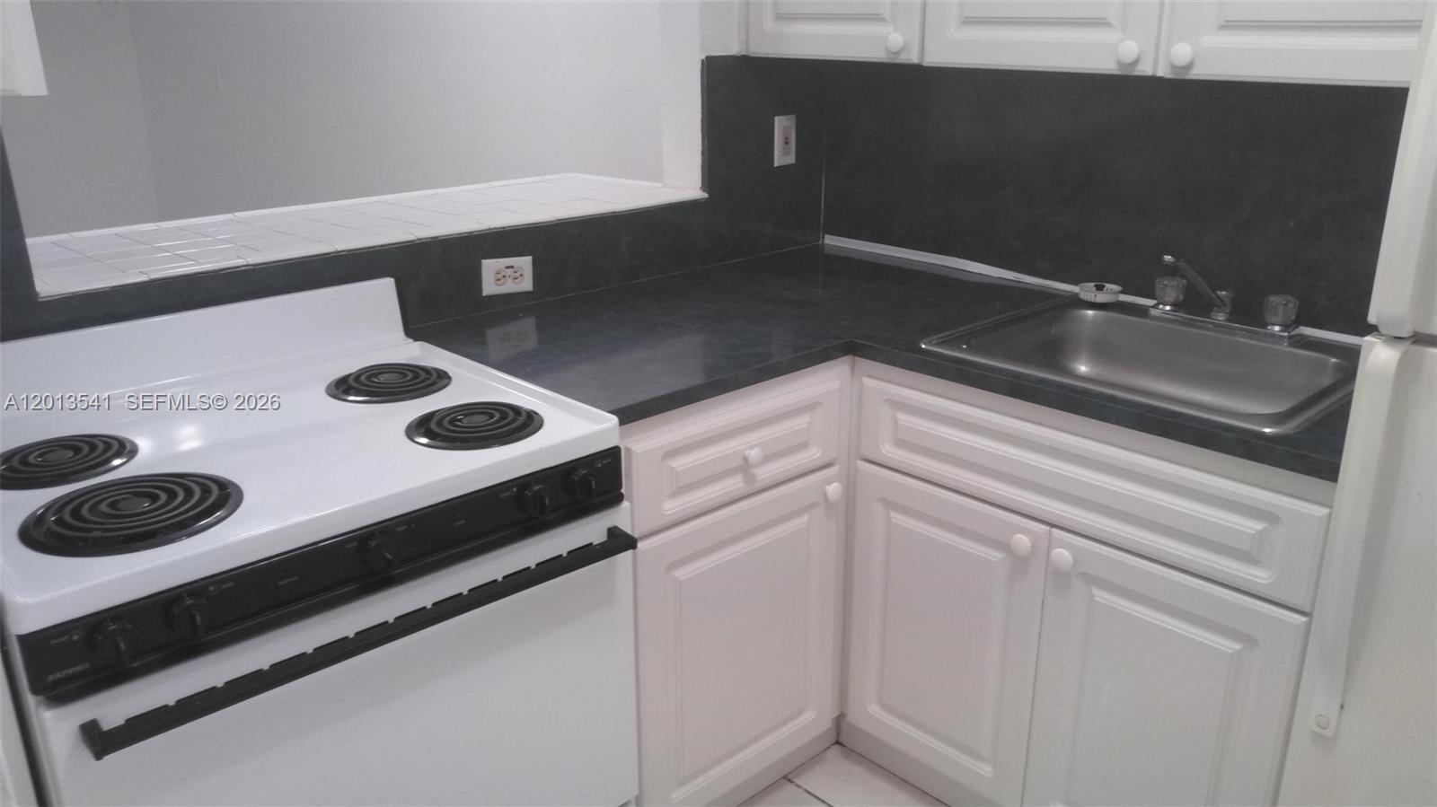A kitchen features white cabinets, a black countertop, a stainless steel sink, and a stove — 1441 Lincoln Rd # 414, Miami Beach FL 33139, MIAMI BEACH, FL