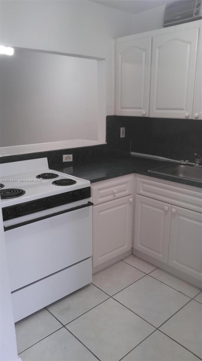 A kitchen features white cabinets, a white electric stove, and dark countertops — 1441 Lincoln Rd # 414, Miami Beach FL 33139, MIAMI BEACH, FL