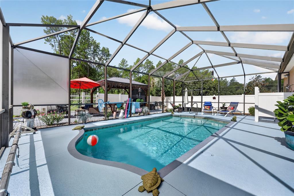 A screened-in swimming pool area with a patio, lounge chairs, and a gazebo in the background — 20096 SW 59TH LANE, DUNNELLON, FL