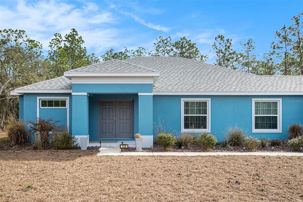 A single-story blue house with a covered entryway and two windows on the front facade — 128 CYPRESS BOULEVARD E, HOMOSASSA, FL