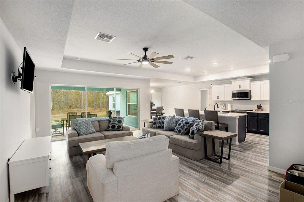 An open-concept living room and kitchen featuring light wood-look flooring and a tray ceiling — 128 CYPRESS BOULEVARD E, HOMOSASSA, FL
