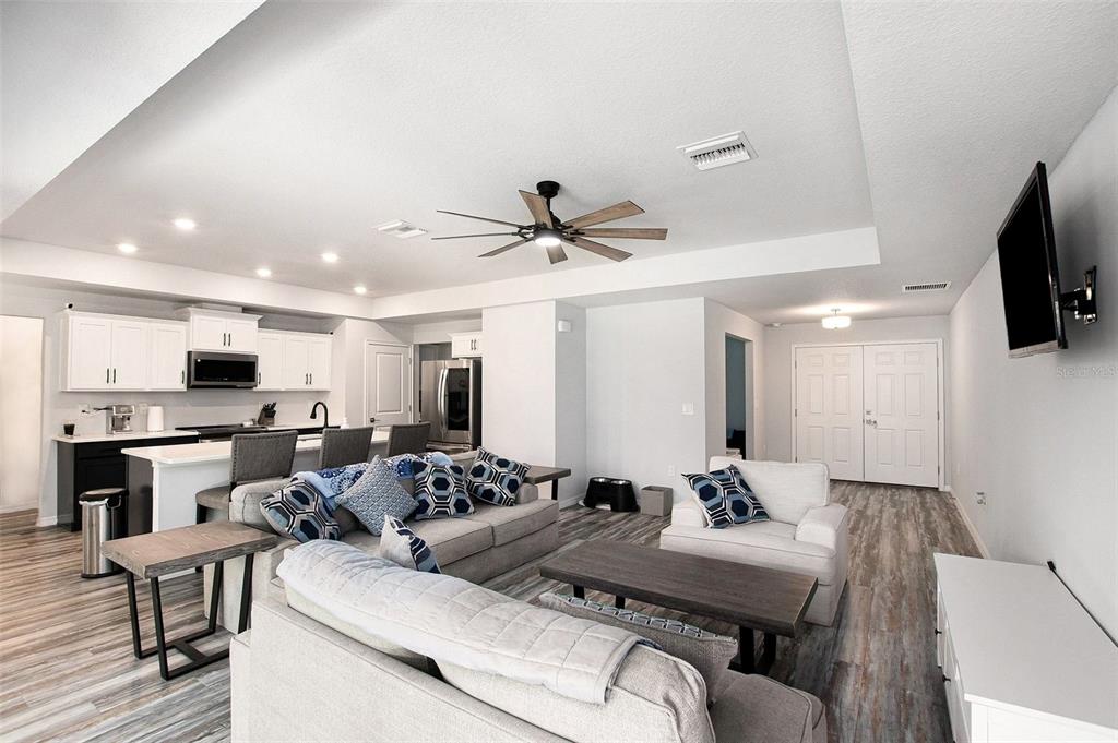 An open-concept living room and kitchen featuring light wood-look flooring and white cabinetry — 128 CYPRESS BOULEVARD E, HOMOSASSA, FL