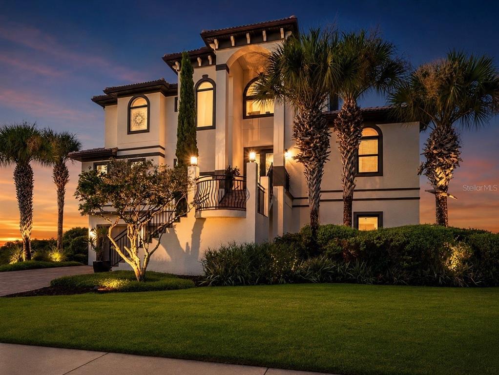 A multi-story Mediterranean-style house with a balcony and palm trees at sunset — 7 HAMMOCK BEACH CIRCLE S, PALM COAST, FL
