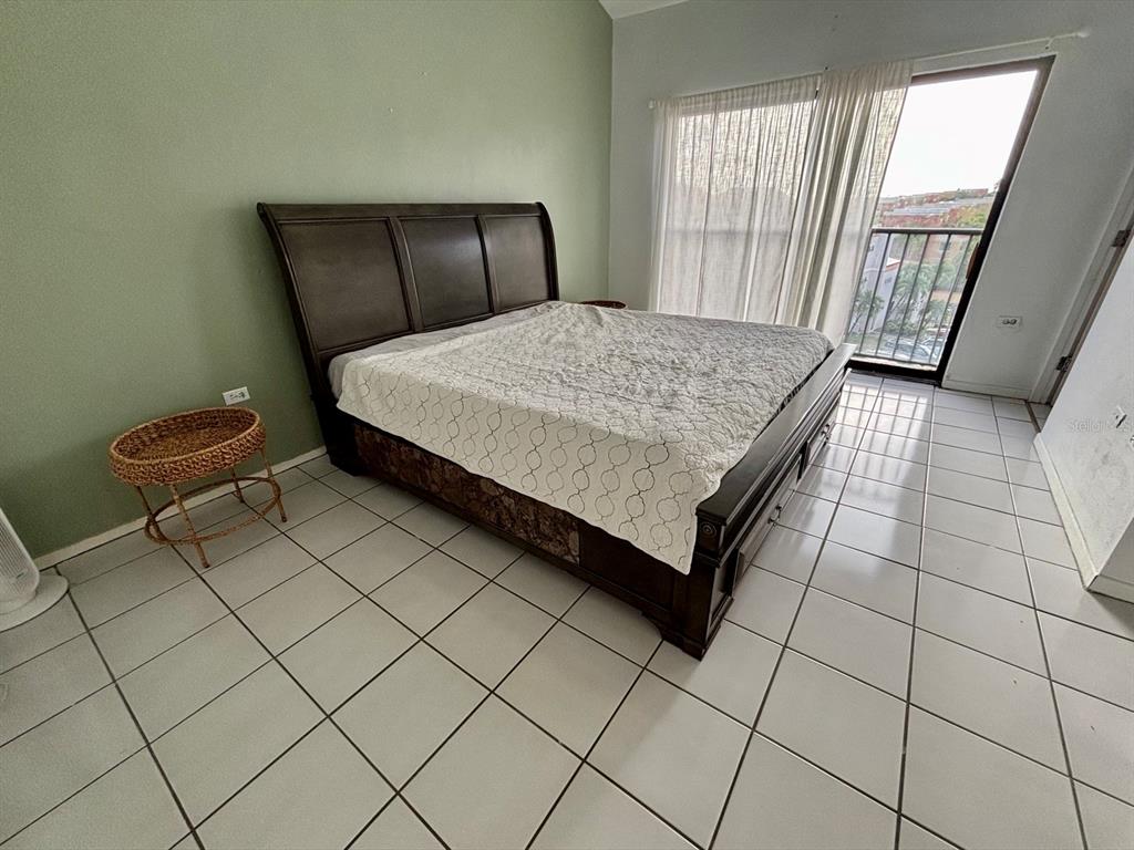 A bedroom with a dark wood bed frame, light tile flooring, and a sliding glass door — 150 PALMAS DRIVE UNIT 118, HUMACAO, PR