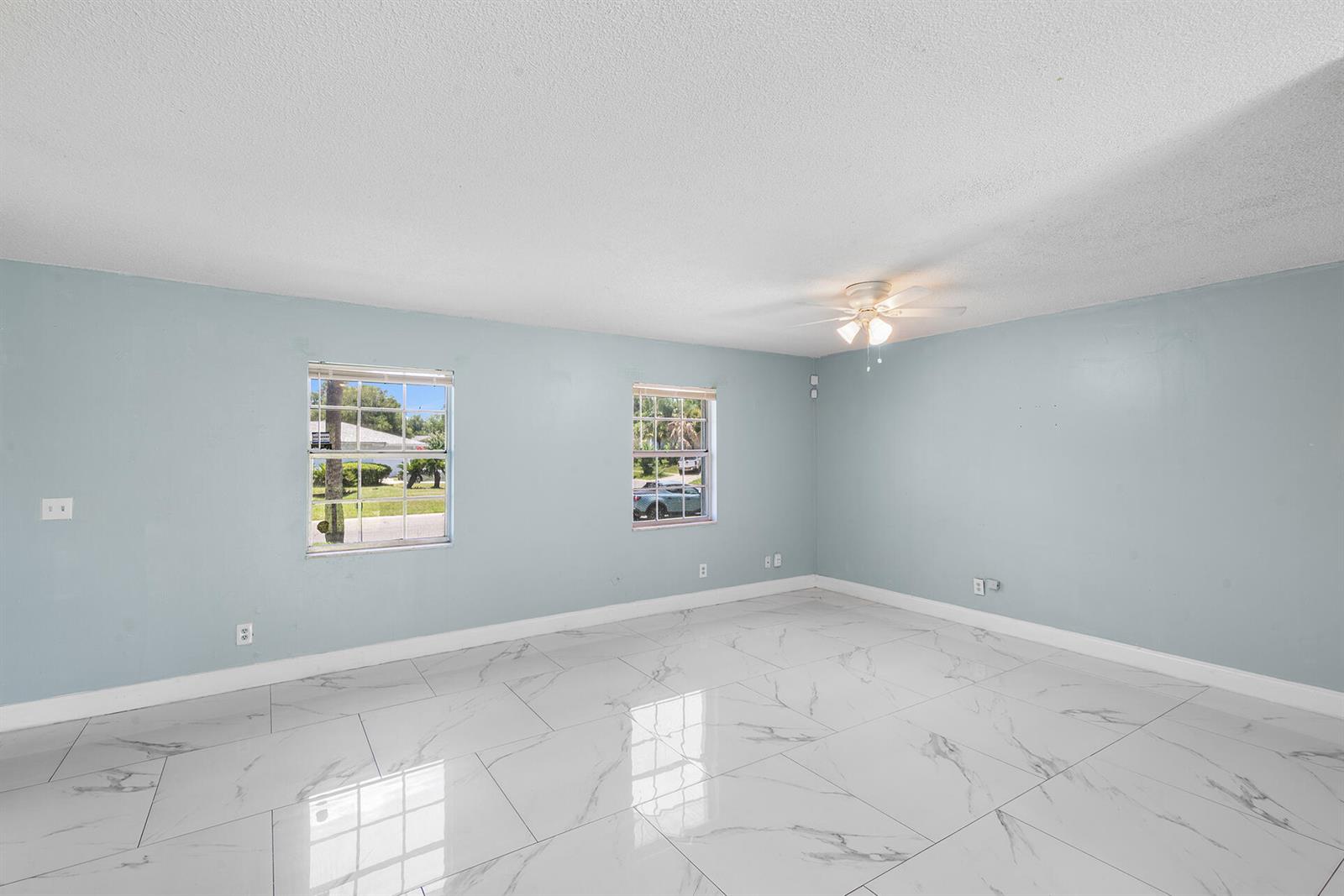 An empty room features light blue walls, white marble-look tile flooring, and two windows — 2137 San Jose Boulevard, Orlando FL 32808, ORLANDO, FL