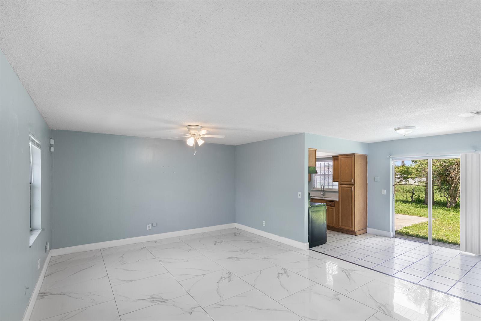 A living room with light blue walls, white marble-look tile flooring, and an adjacent kitchen — 2137 San Jose Boulevard, Orlando FL 32808, ORLANDO, FL