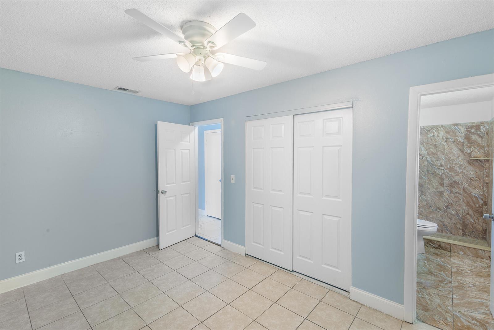 A bedroom with light blue walls, tile flooring, a ceiling fan, and an attached bathroom — 2137 San Jose Boulevard, Orlando FL 32808, ORLANDO, FL