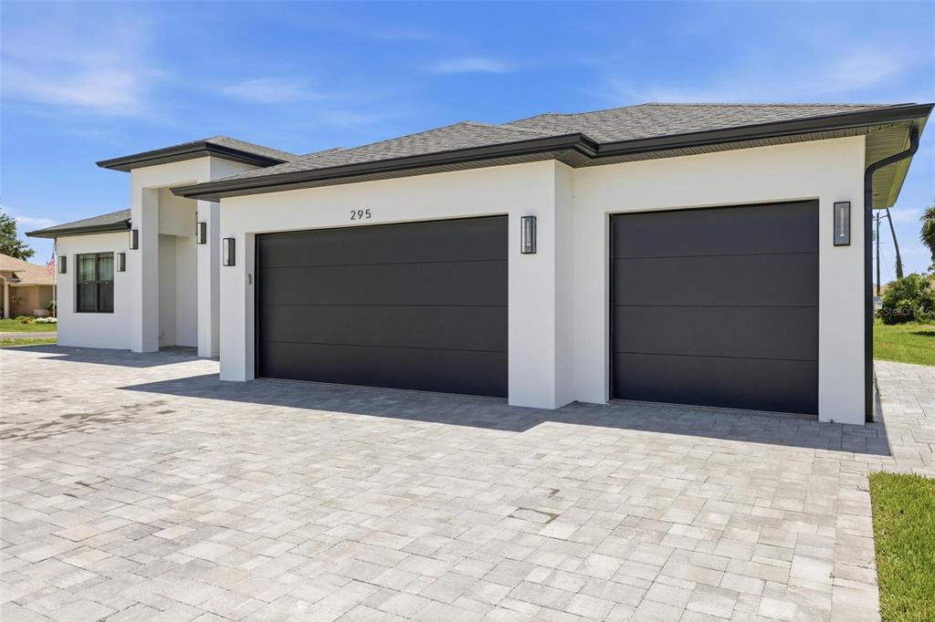 A modern house exterior features a three-car garage with dark doors and a paved driveway — 295 WHITE MARSH LANE, ROTONDA WEST, FL