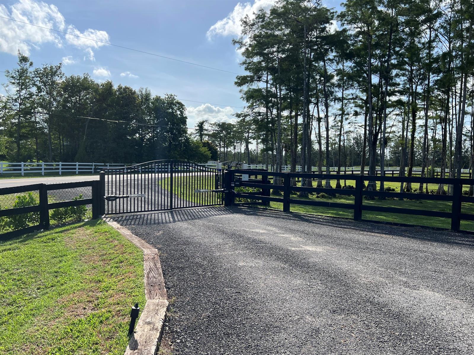 A black metal driveway gate opens onto a gravel path bordered by wooden landscaping timbers — 6600 Duckweed Road, Wellington FL 33449, WELLINGTON, FL