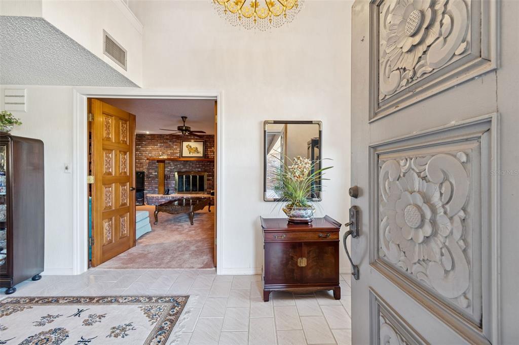 An entryway with a carved wooden door, tiled floor, and a view into a living room — 29244 WHIPPORWILL LANE, WESLEY CHAPEL, FL