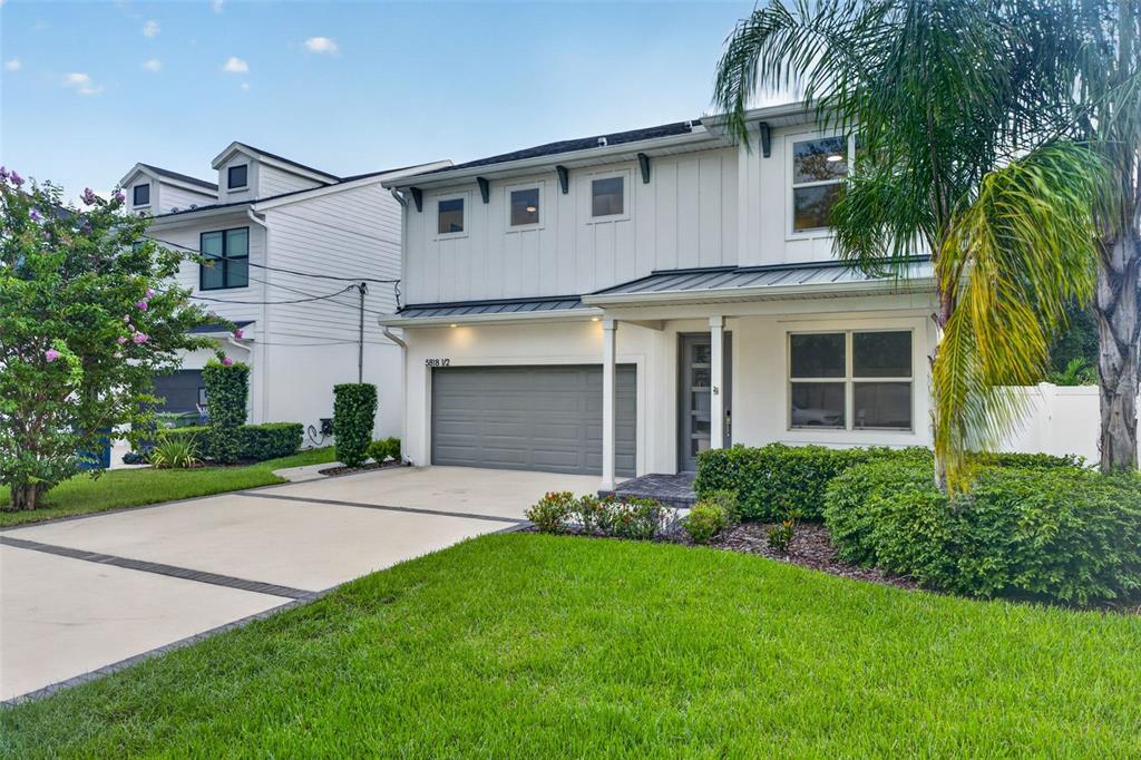 A two-story house with white vertical siding, a gray garage, and a landscaped front yard — 5818 1/2 S 6TH STREET, TAMPA, FL