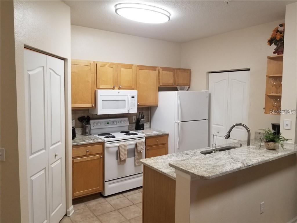 A kitchen features light wood cabinets, granite countertops, white appliances, and a breakfast bar — 4207 S DALE MABRY HIGHWAY UNIT 10207, TAMPA, FL